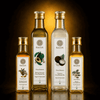 Four Kaizer branded glass bottles of cold pressed oils arranged on a reflective dark surface against a black background with warm golden light.