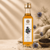 A bottle of Kaizer Kalonji Oil (black seed oil) centered on a styled background with text callouts on the left, dried flowers, a wooden bowl of black seeds, and a beige fabric cloth.