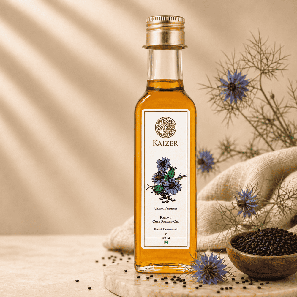 A bottle of Kaizer Kalonji Oil (black seed oil) centered on a styled background with text callouts on the left, dried flowers, a wooden bowl of black seeds, and a beige fabric cloth.