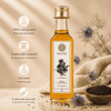 A bottle of Kaizer Kalonji Oil (black seed oil) centered on a styled background with text callouts on the left, dried flowers, a wooden bowl of black seeds, and a beige fabric cloth.