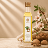 A bottle of Kaizer almond oil stands on a wooden board with almonds, burlap, and pink blossoms around it. 