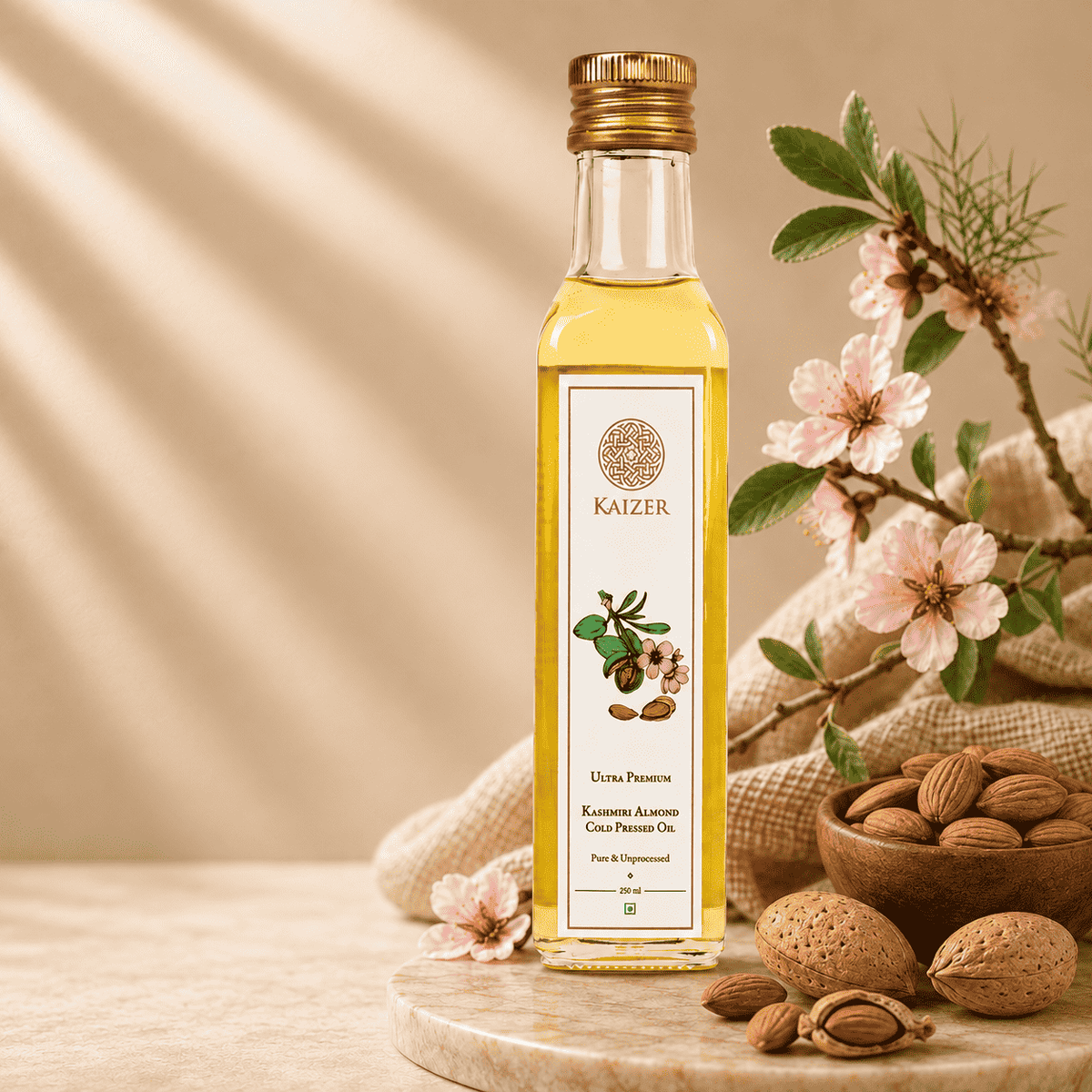 A bottle of Kaizer almond oil stands on a wooden board with almonds, burlap, and pink blossoms around it. 