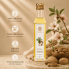 A bottle of Kaizer almond oil stands on a wooden board with almonds, burlap, and pink blossoms around it. Text on the left highlights cold-pressed purity, traditional extraction, lab testing, and kitchen/skincare readiness.