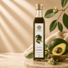A bottle of Kaizer Kenyan Avocado Oil stands on a wooden board next to whole and sliced avocados in a bowl, with warm beige fabric and leafy branches in the background.