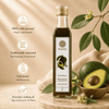 A bottle of Kaizer Kenyan Avocado Oil stands on a wooden board next to whole and sliced avocados in a bowl, with warm beige fabric and leafy branches in the background. Text on the left highlights key product benefits: 100% cold-pressed virgin oil, traditionally extracted, lab tested, and suitable for everyday cooking.
