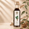 A bottle of Kaizer Malkangani Oil stands on a wooden surface with decorative leaves, berries, and a small bowl of seeds. Text on the left highlights key product benefits: 100% cold-pressed, traditionally extracted, lab tested, and traditionally used for scalp massage.